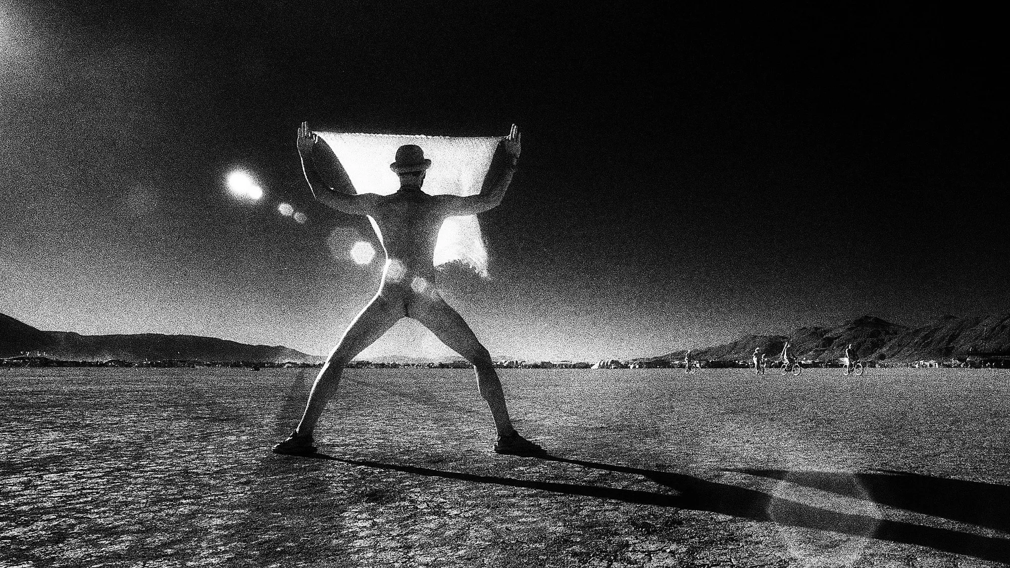 On the Burning Man playa a figure lifts a sheet of light-catching cloth, black-and-white infrared